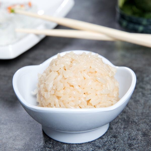 A white scallop shaped melamine bowl filled with rice with chopsticks on top.