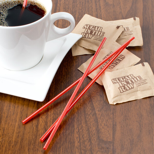 A cup of coffee with red Choice coffee stirrers and sugar packets on a table.
