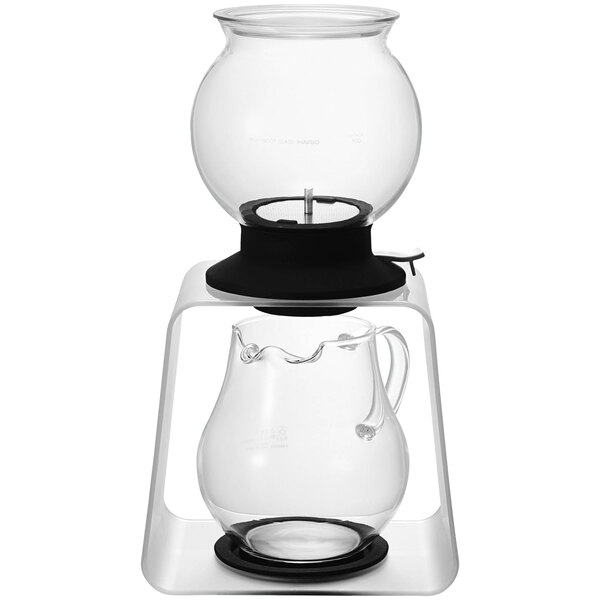 A Hario glass tea dripper with glass pitcher on a black surface.