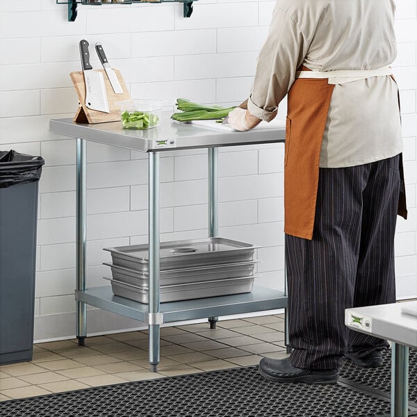 A person standing in a kitchen at a Regency stainless steel work table.