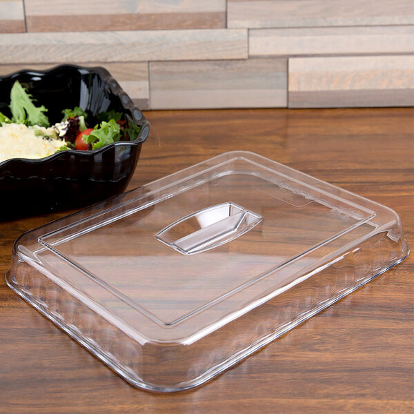 A clear plastic lid on a black Deli Crock filled with salad on a counter.