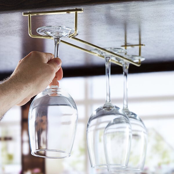 A hand using a Regency brass plated glass hanger to hold wine glasses.