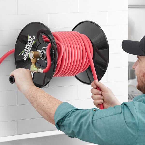 A man using a Regency powder-coated steel hose reel to spray water on a wall.