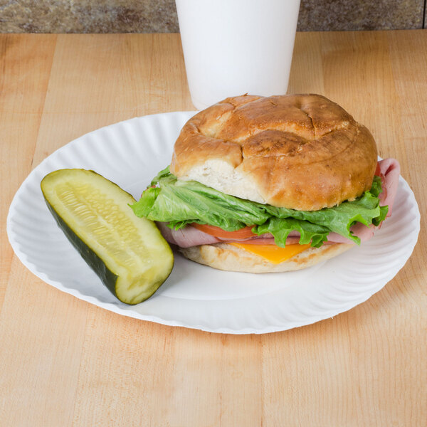 A sandwich and a pickle on a Choice white uncoated paper plate.