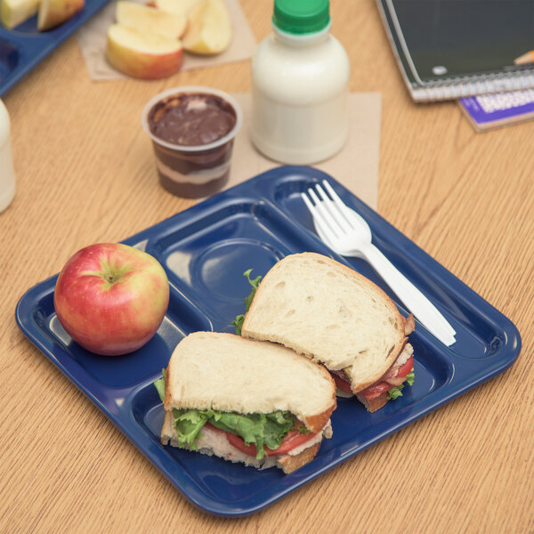 A Carlisle dark blue 4 compartment tray with a sandwich and apple on it.