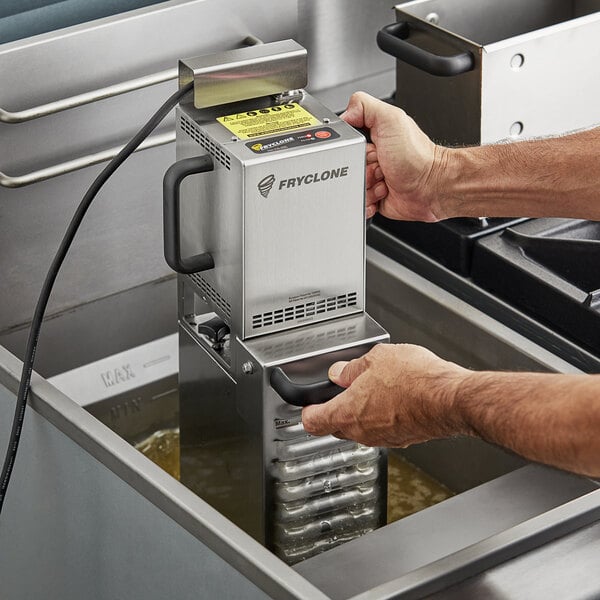 A man using a Fryclone portable fryer oil filter machine on a professional kitchen counter.