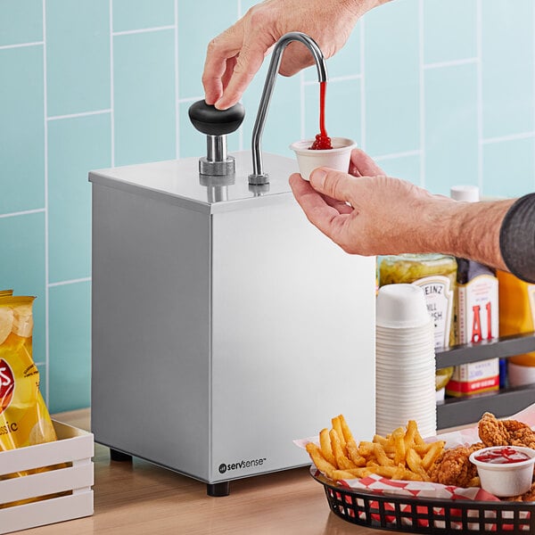 A person using a ServSense stainless steel condiment pump to pour ketchup into a cup.