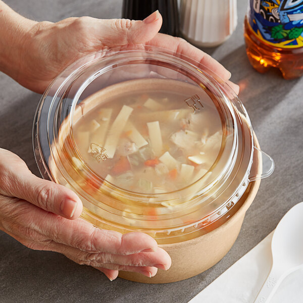 Hands holding a Choice PET take-out lid on a plastic container of soup.