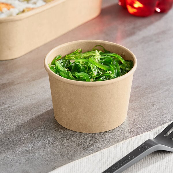 A Choice paper take-out container filled with green seaweed on a table.