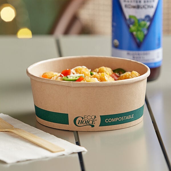 A bowl of food in a Kraft take-out container with a wooden spoon on a table.
