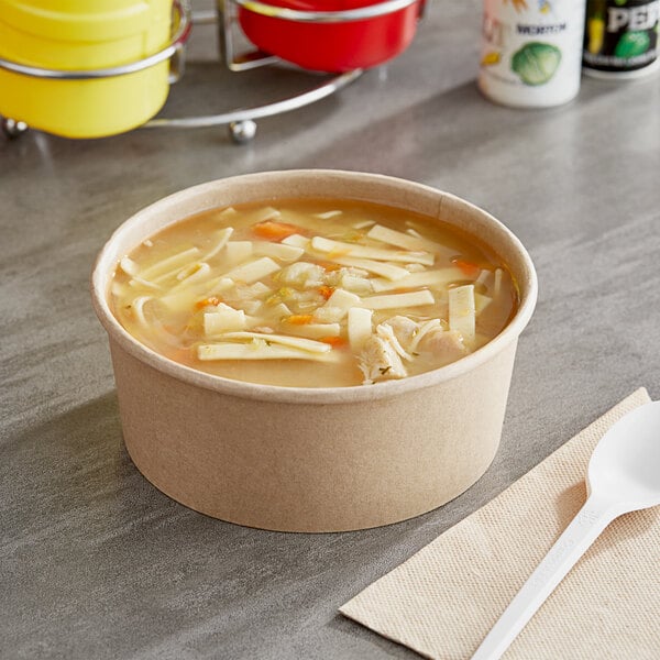 A bowl of soup with noodles in a yellow Choice kraft paper take-out container on a table.
