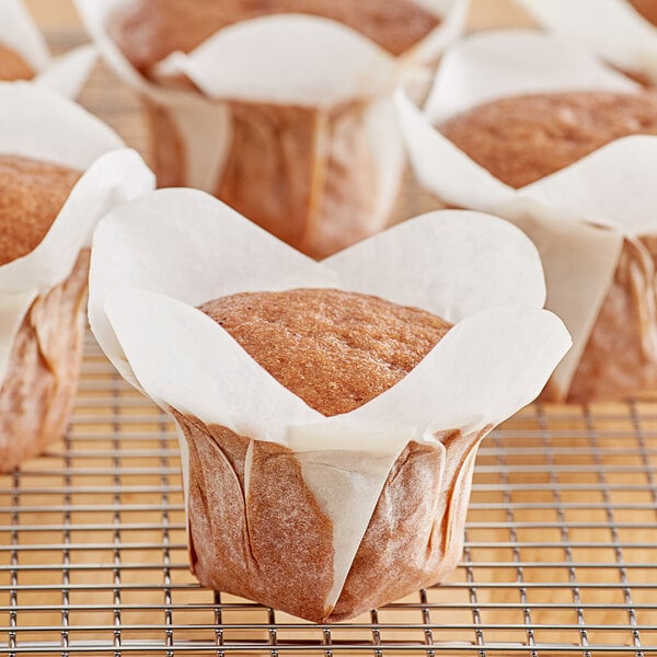 A group of Hoffmaster white lotus baking cups filled with muffins on a cooling rack.
