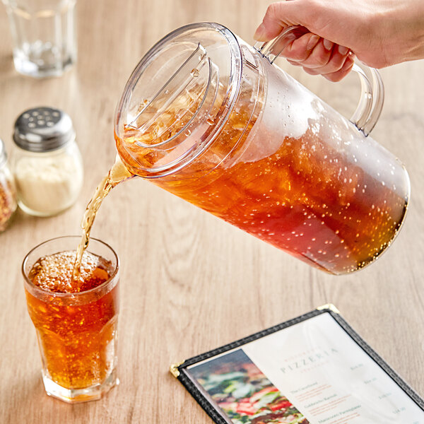 A person pouring brown liquid into a Choice clear polycarbonate beverage pitcher.