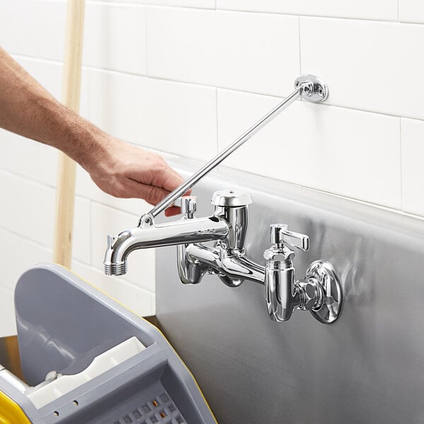 A hand using a tool to install a Chicago Faucets wall-mounted sink faucet over a grey sink.