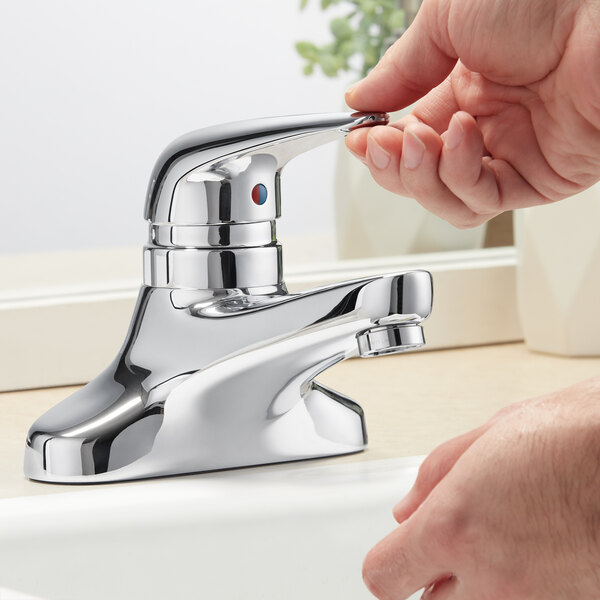A person's hand pressing a button to open a Chicago Faucets deck-mounted sink faucet.