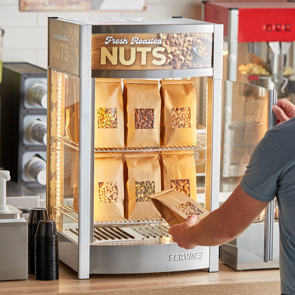 A man putting bags of nuts into a ServIt countertop display warmer.