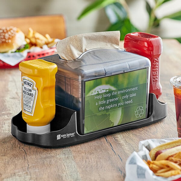 A San Jamar tabletop napkin dispenser with condiments on a table.