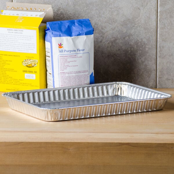 A Durable Packaging aluminum foil 1/4 sheet cake pan on a metal tray with a box of baking mix and a bag of flour.