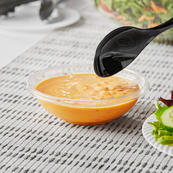 A Visions clear plastic bowl filled with food with a spoon in it.