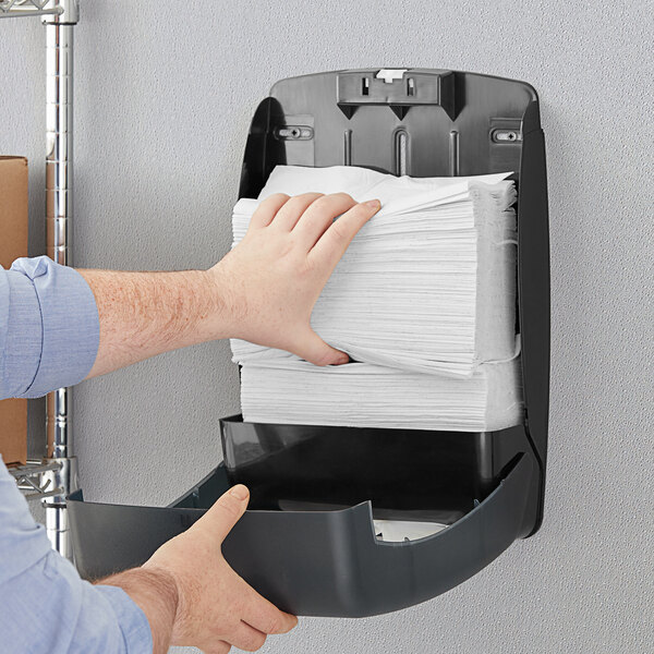 A person reaching for a stack of Tork white multi-fold paper towels.