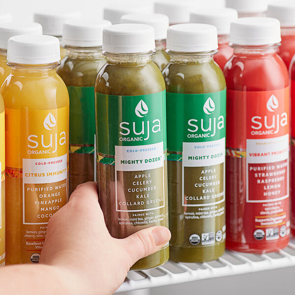 A hand holding a bottle of Suja Mighty Dozen cold-pressed juice.