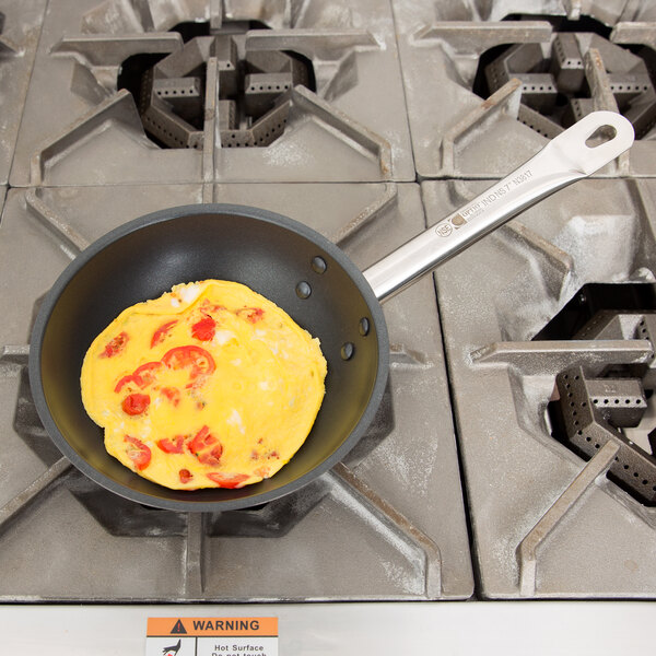 A Vollrath Optio stainless steel non-stick fry pan with an omelet in it on a stove.