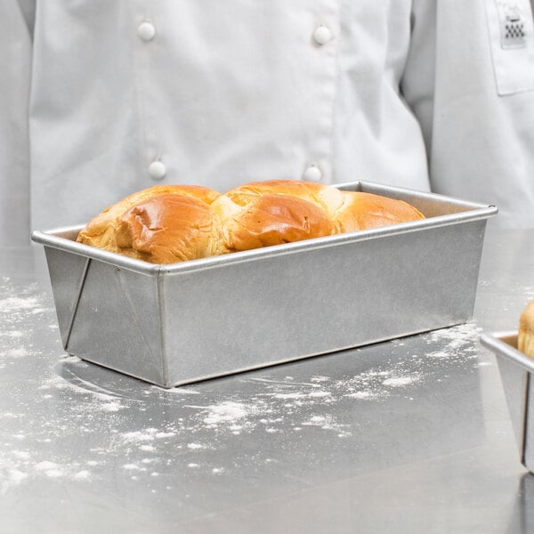 A baker's hand holding a Chicago Metallic bread loaf pan filled with bread.