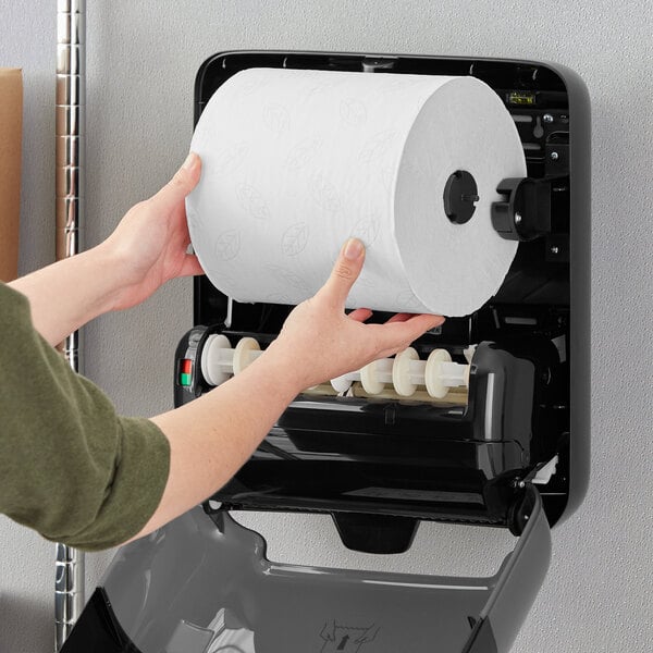 A person holding a roll of Tork Advanced Matic white paper towels with a grey leaf pattern.