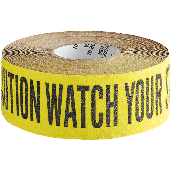 A roll of yellow Wooster safety tape with black text reading "Caution Watch Your Step"