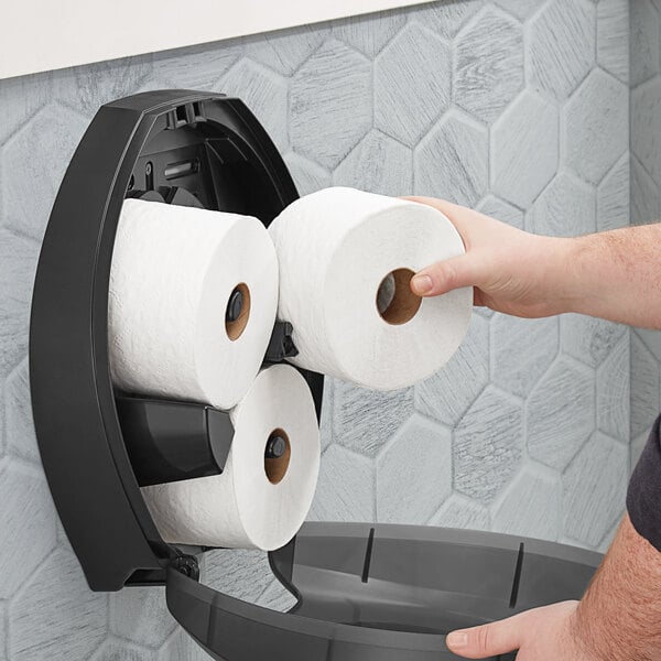 A hand holds a Tork Universal toilet paper roll in a holder.