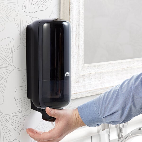 A person using a black Tork manual foam hand soap dispenser.