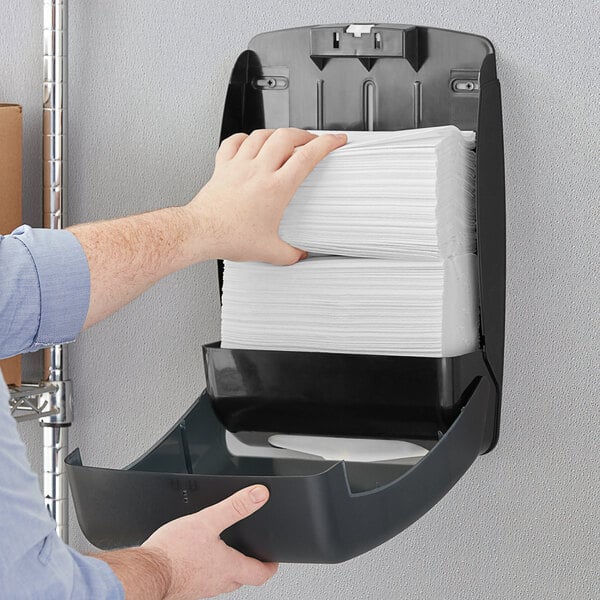 A hand holding a stack of Tork white multi-fold paper towels.