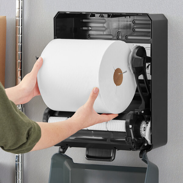 A person holding a roll of Tork white notched paper towels.