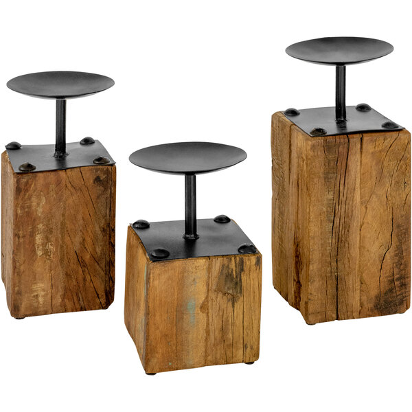 Three wooden candle holders with black metal bases on a wooden block.