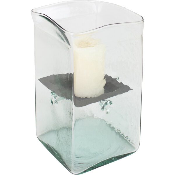 A Kalalou small glass square hurricane candle holder with a white candle inside on a rustic metal insert.