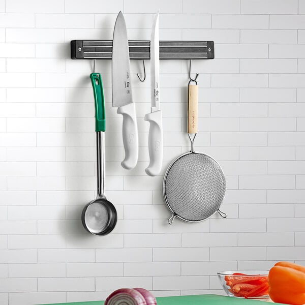 A white wall with a Choice 13" Magnetic Knife Holder with kitchen utensils hanging from it.