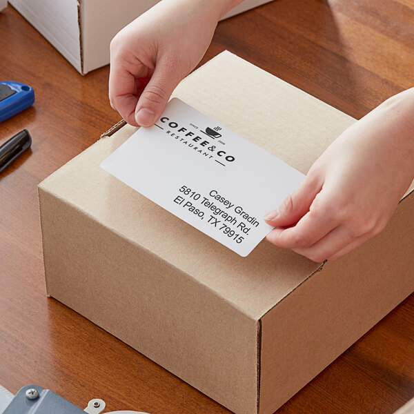 A person holding a Lavex white mailing label with a business card on a box.