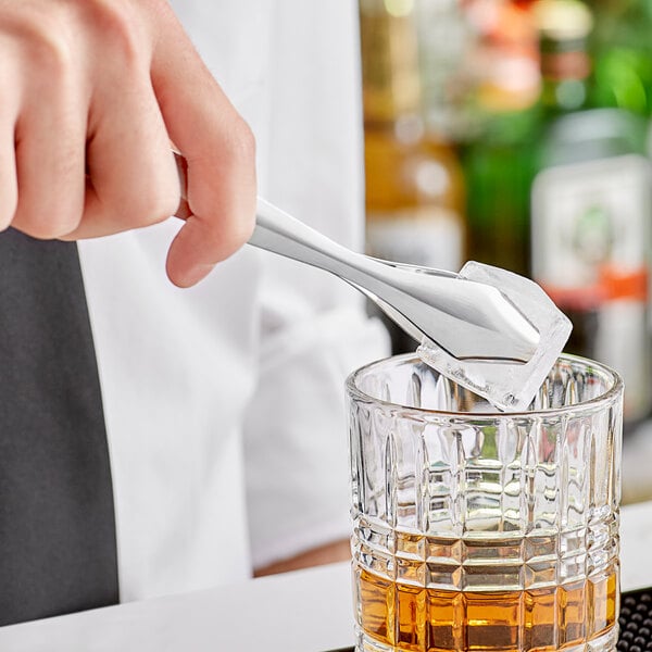 A person using a Barfly stainless steel ice tong to add ice to a glass of alcohol.