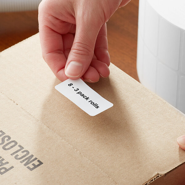 A hand using a Lavex white thermal label to put on a cardboard box.