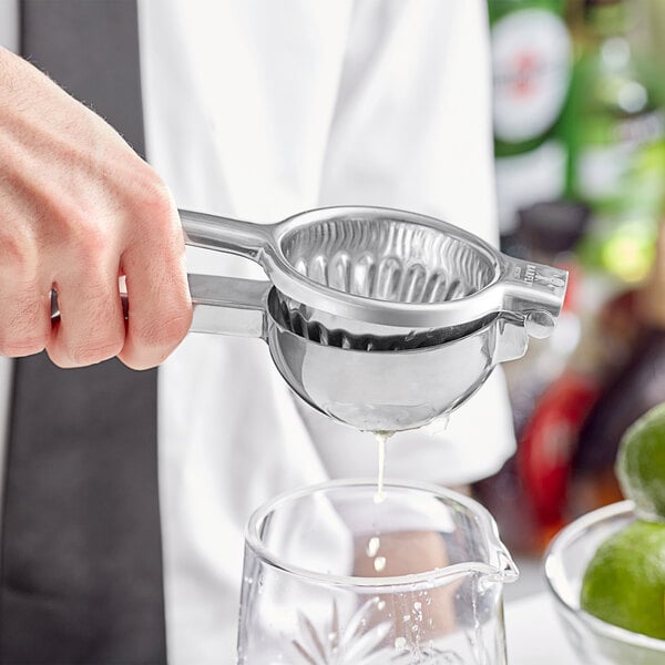 A person using a Barfly stainless steel juicer to pour lime juice into a glass.