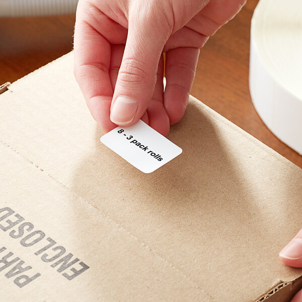 A person's hand holding a small white Lavex label and putting it on a cardboard box.