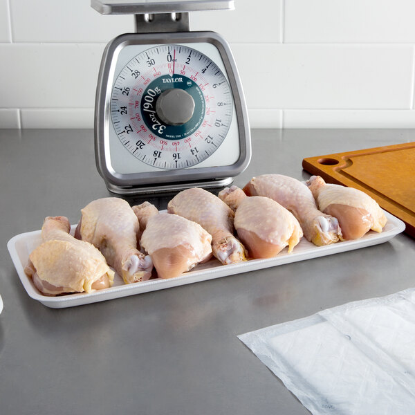 A white CKF foam tray holding raw chicken legs on a kitchen counter.