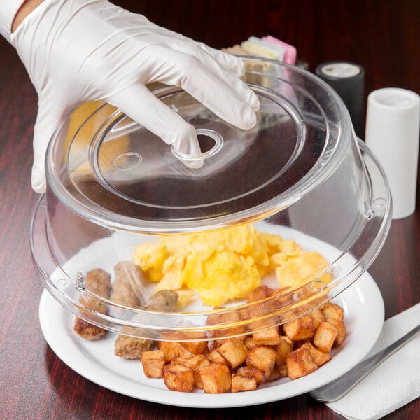 A person in white gloves using a Cambro clear plastic lid to cover a plate of food.