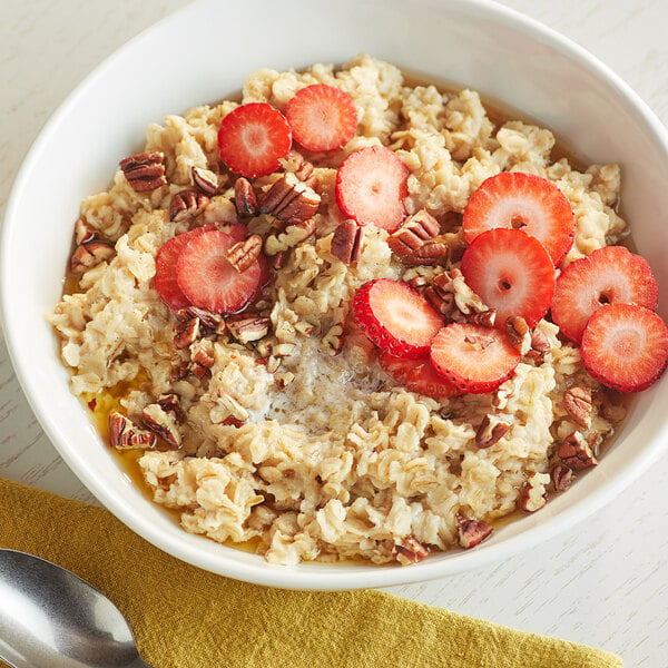 A bowl of Bob's Red Mill whole grain rolled oats topped with strawberries and pecans on a white background with a spoon.