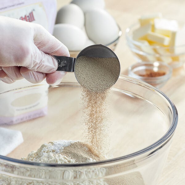 A person pouring Bob's Red Mill Gluten-Free Active Dry Yeast into a bowl of flour.