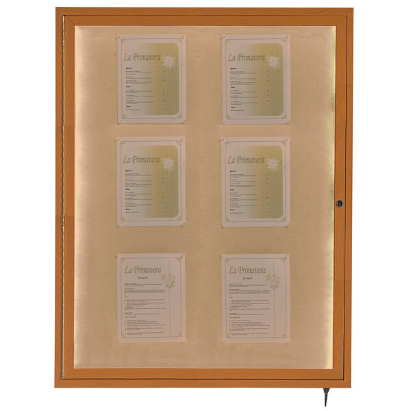 An oak finish Aarco bulletin board cabinet with papers inside.