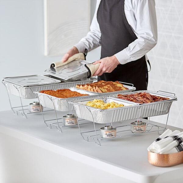 A person in an apron serving food from a Choice disposable chafer dish kit on a table.