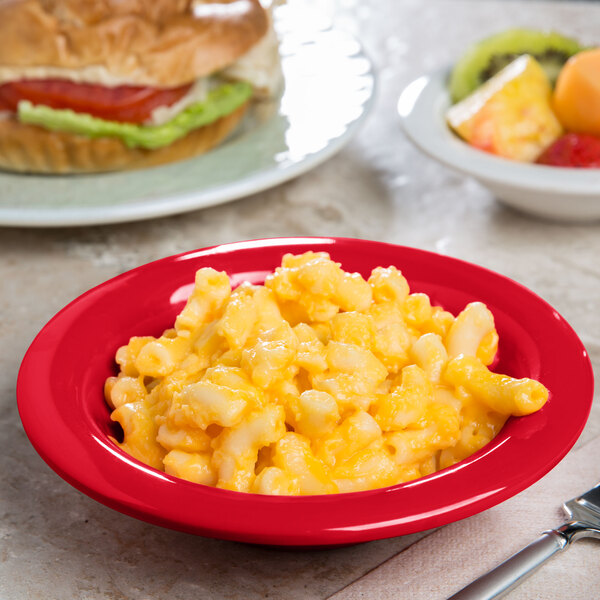 A bowl of macaroni and cheese with a sandwich on a table.