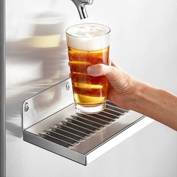 A hand holding a glass of beer under a Regency wall mount beer drip tray.