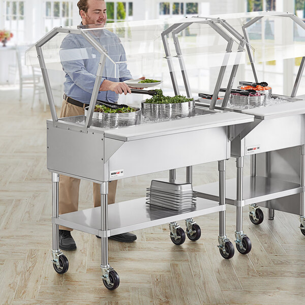 A man using a ServIt stainless steel ice-cooled food table with a sneeze guard.